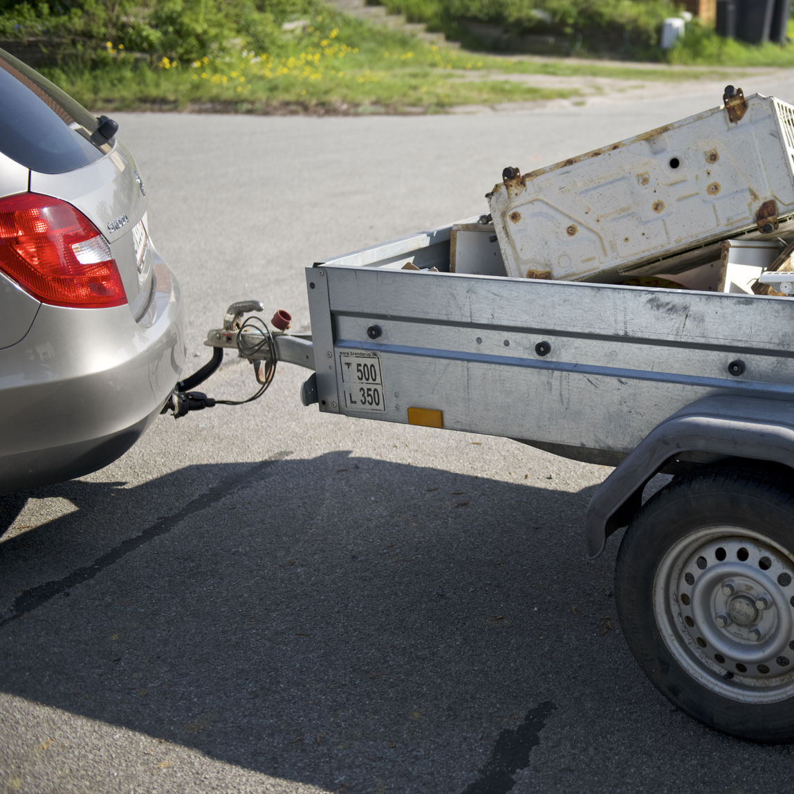 Trailer fyldt med gammelt elektronik og metaldele, tilkoblet en bil. Traileren er klar til at blive kørt til genbrugspladsen for korrekt affaldssortering og genbrug