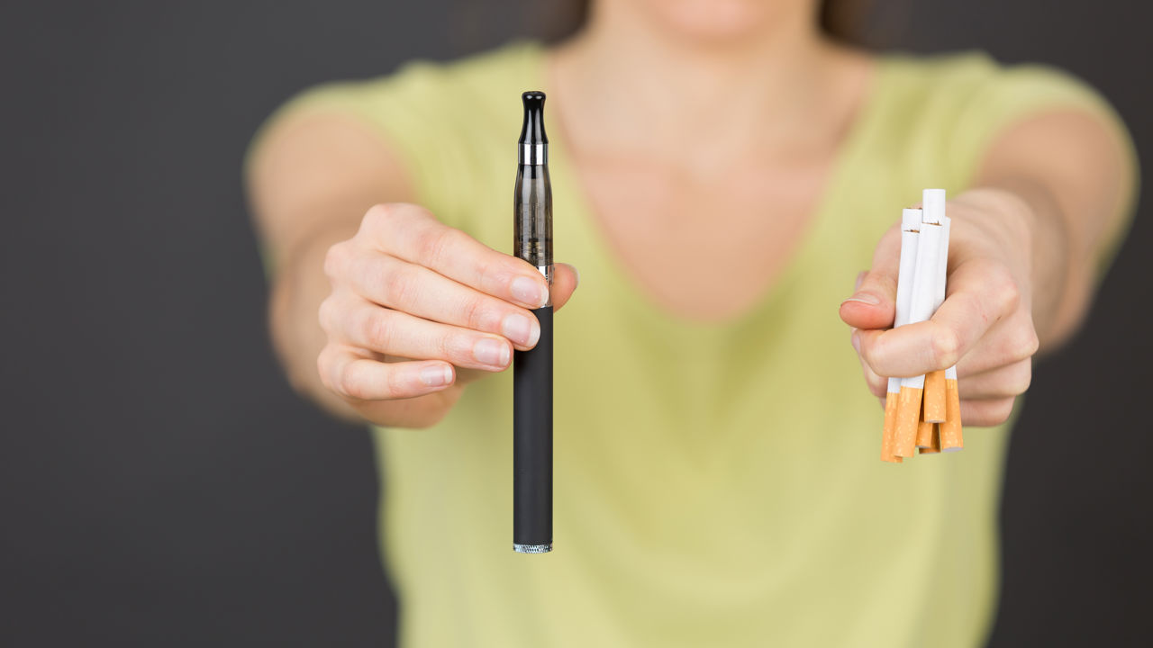Foto af person der holder cigaretter og e-cigaret i hænderne