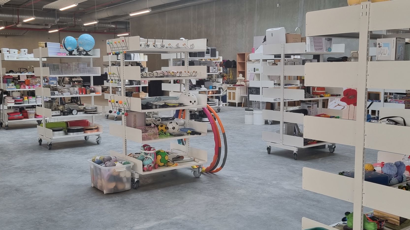 Foto af genbrugsbutikken på RessourceCenter Vejle. Rummet er fyldt med hylder, der indeholder forskellige genbrugsvarer som køkkenudstyr, legetøj, bøger og andre brugte effekter, der er gratis for borgere at tage med hjem