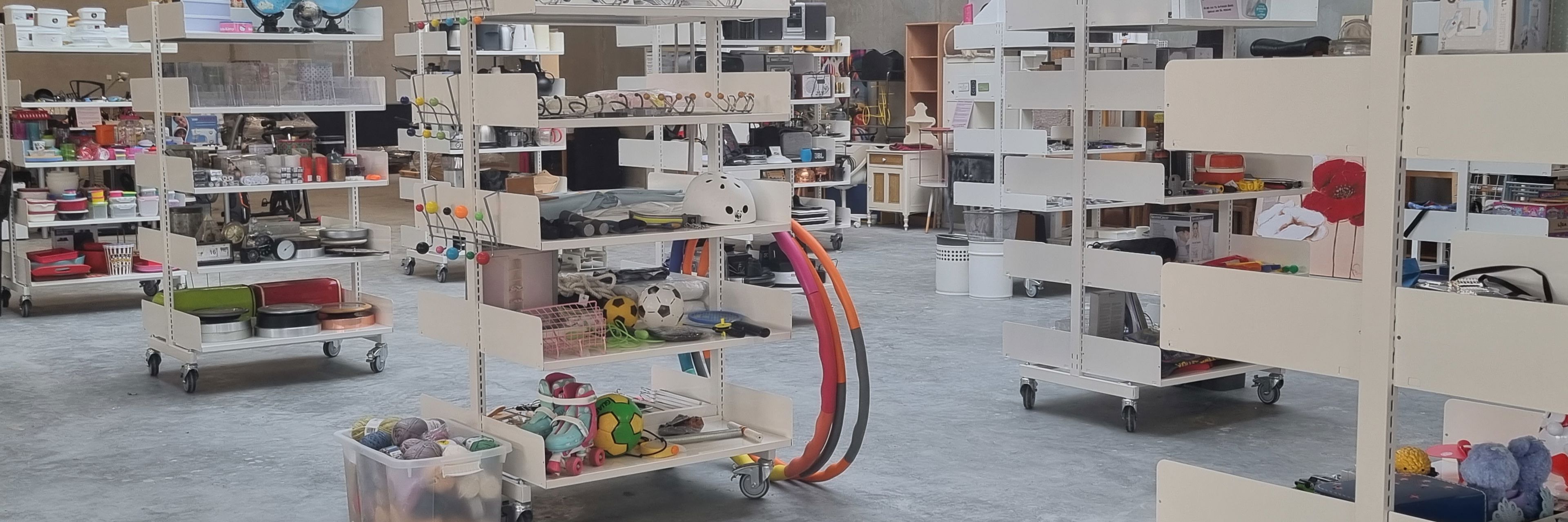 Foto af genbrugsbutikken på RessourceCenter Vejle. Rummet er fyldt med hylder, der indeholder forskellige genbrugsvarer som køkkenudstyr, legetøj, bøger og andre brugte effekter, der er gratis for borgere at tage med hjem