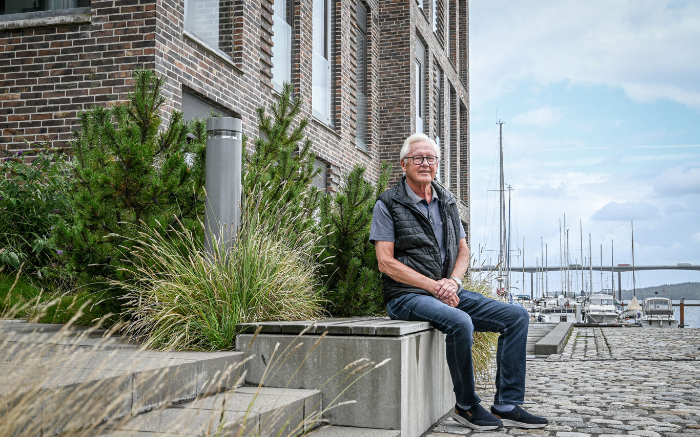 Leif sidder på en bænk foran boligområdet på Havneøen med lystbådehavnen i baggrunden.