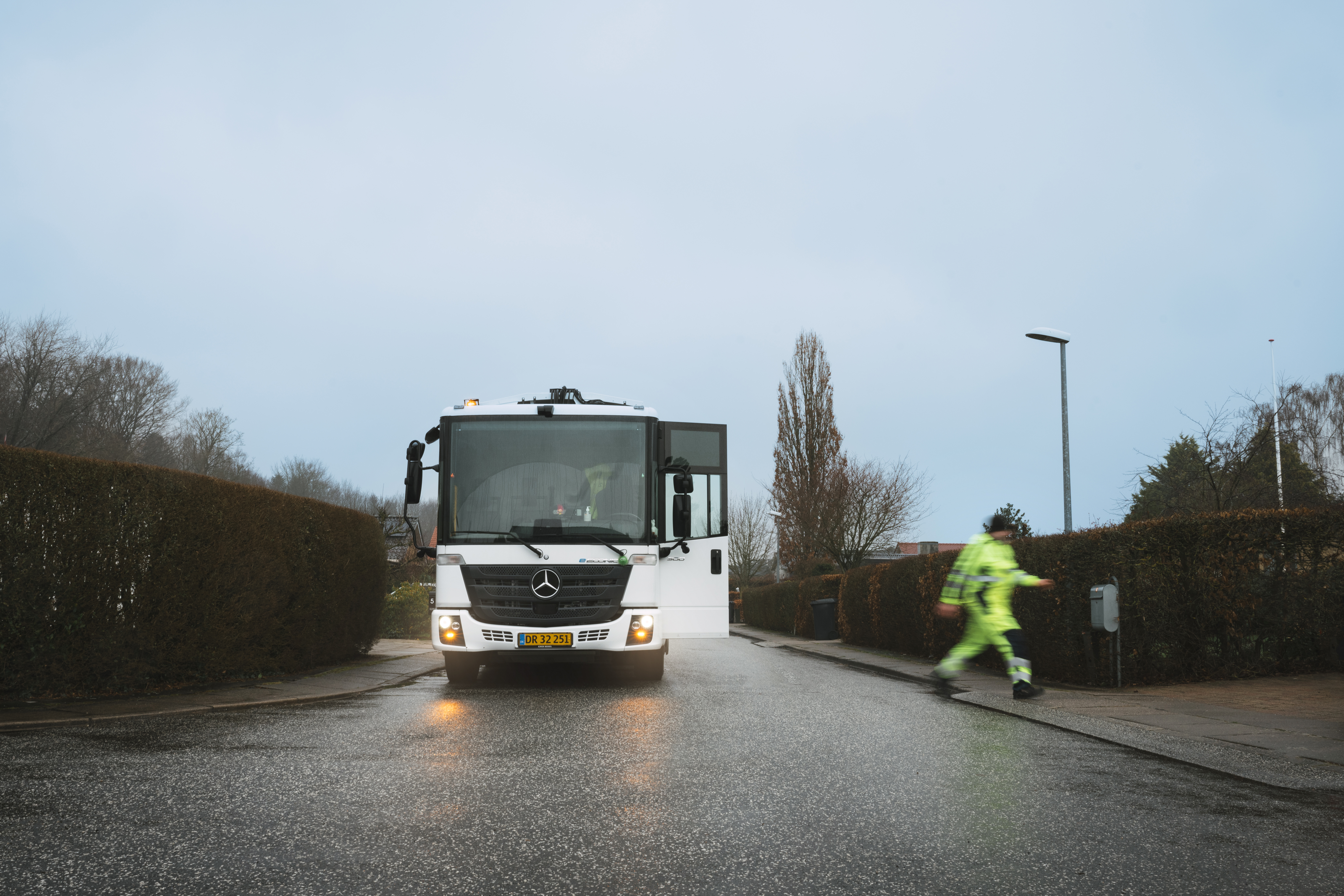 Skraldebil set forfra på en regnfuld dag, mens en skraldemand krydser vejen