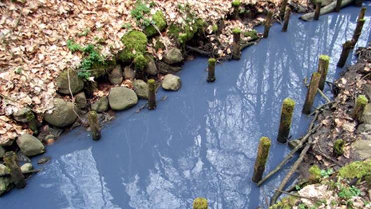 Blå maling hældt i en vejrist, som er endt i et vandløb.