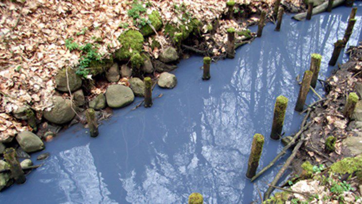 Blå maling hældt i en vejrist, som er endt i et vandløb.