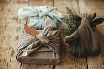 Tre julegaver pakket ind i stof med grene og blade – furoshiki-inspireret, bæredygtig indpakning.