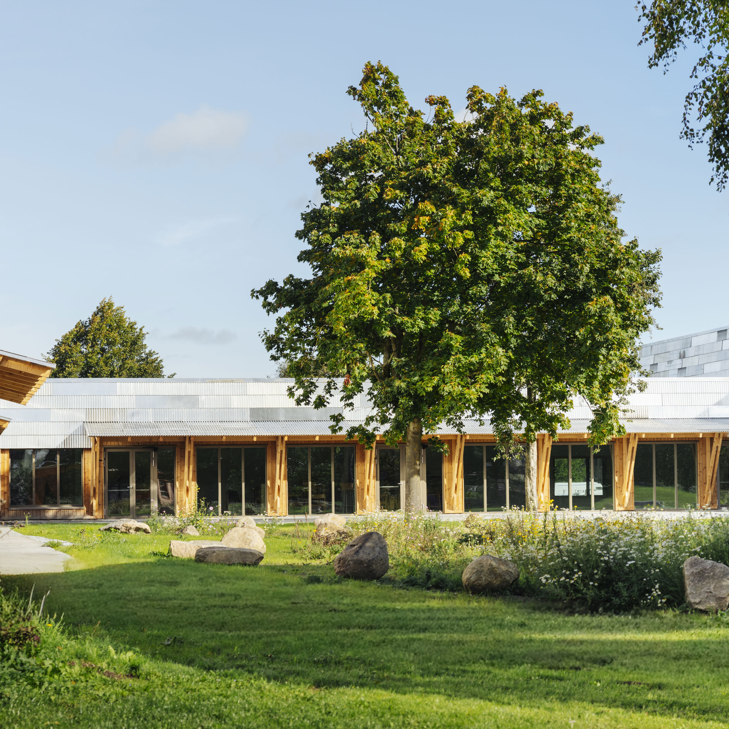 Foto viser ENGEN - Kulturhus & Bibliotek udefra. Der står et stort træ og masser grønt og blomster ude foran kulturhuset.
