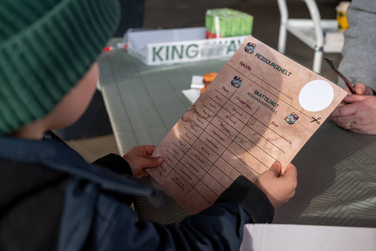 Barn står med papir i hånden, hvorpå der står "ressourcehelt" som en del af skattejagt på Torvet ved RessourceCenter Vejle i forbindelsen med fejringen af RCV's 2-års fødselsdag-