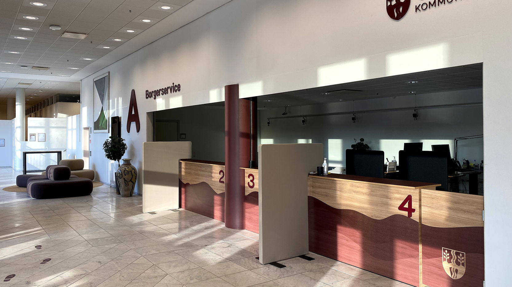 Receptionen i Borgerservice i Vejle Kommune med flere betjeningsskranker markeret med numrene 2, 3 og 4 samt skiltning på væggen, der viser kommunens logo.