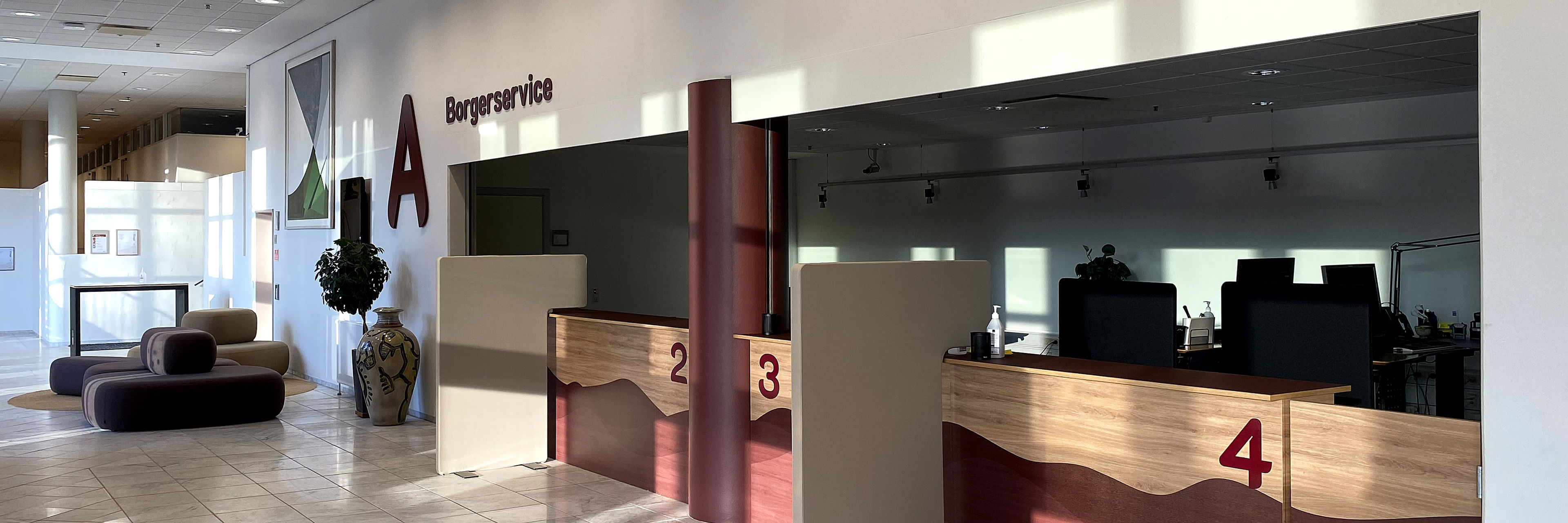 Receptionen i Borgerservice i Vejle Kommune med flere betjeningsskranker markeret med numrene 2, 3 og 4 samt skiltning på væggen, der viser kommunens logo.