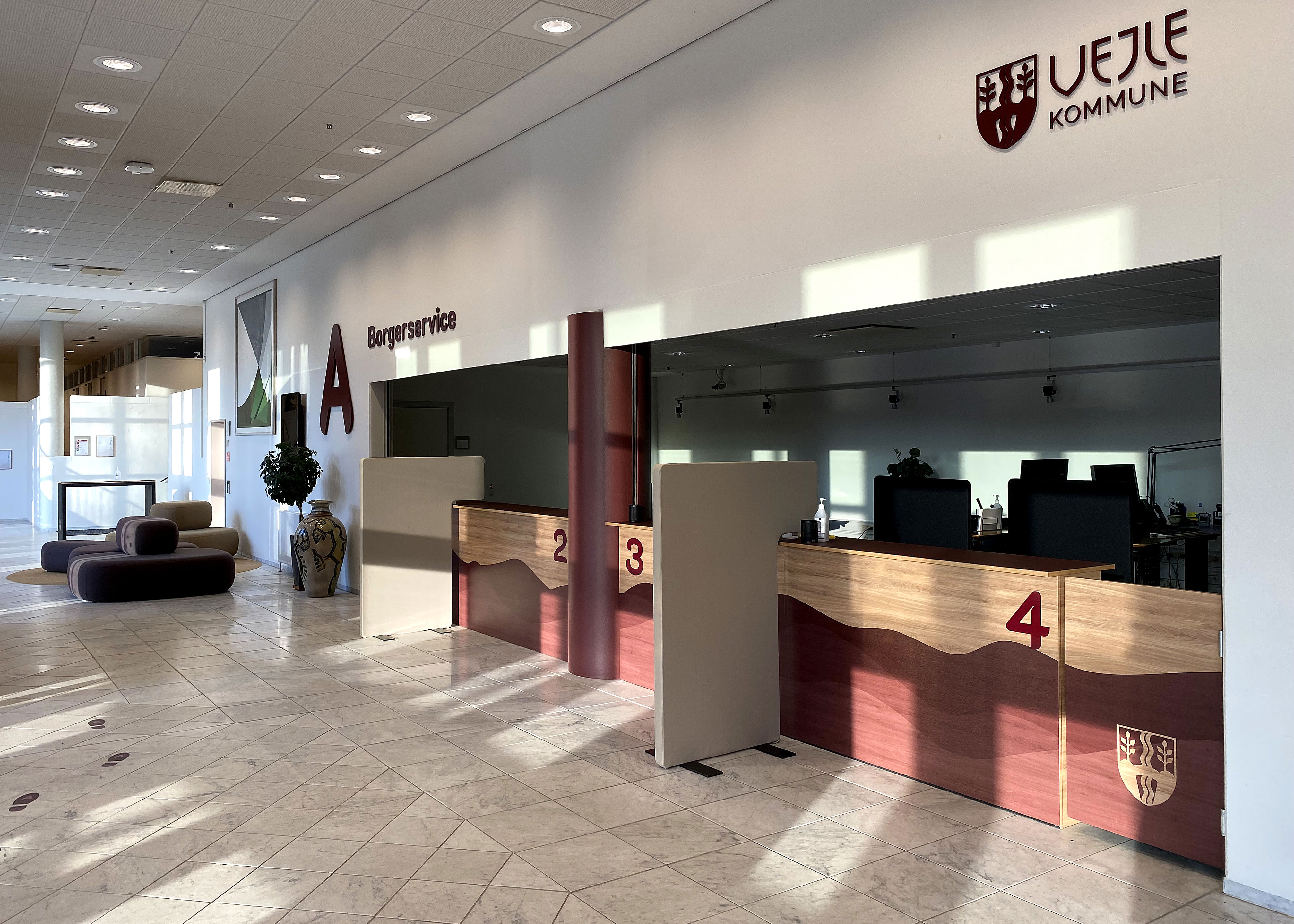 Receptionen i Borgerservice i Vejle Kommune med flere betjeningsskranker markeret med numrene 2, 3 og 4 samt skiltning på væggen, der viser kommunens logo.