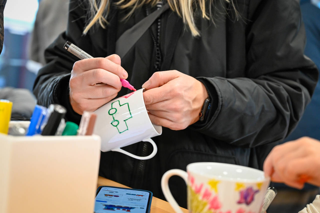 Person iført sort jakke maler med tusch på hvid kop af keramik.