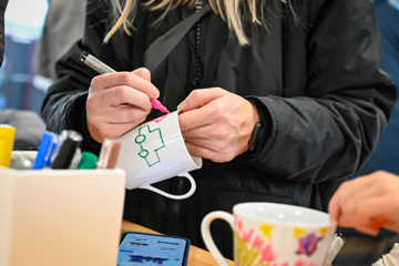 Person iført sort jakke maler med tusch på hvid kop af keramik.