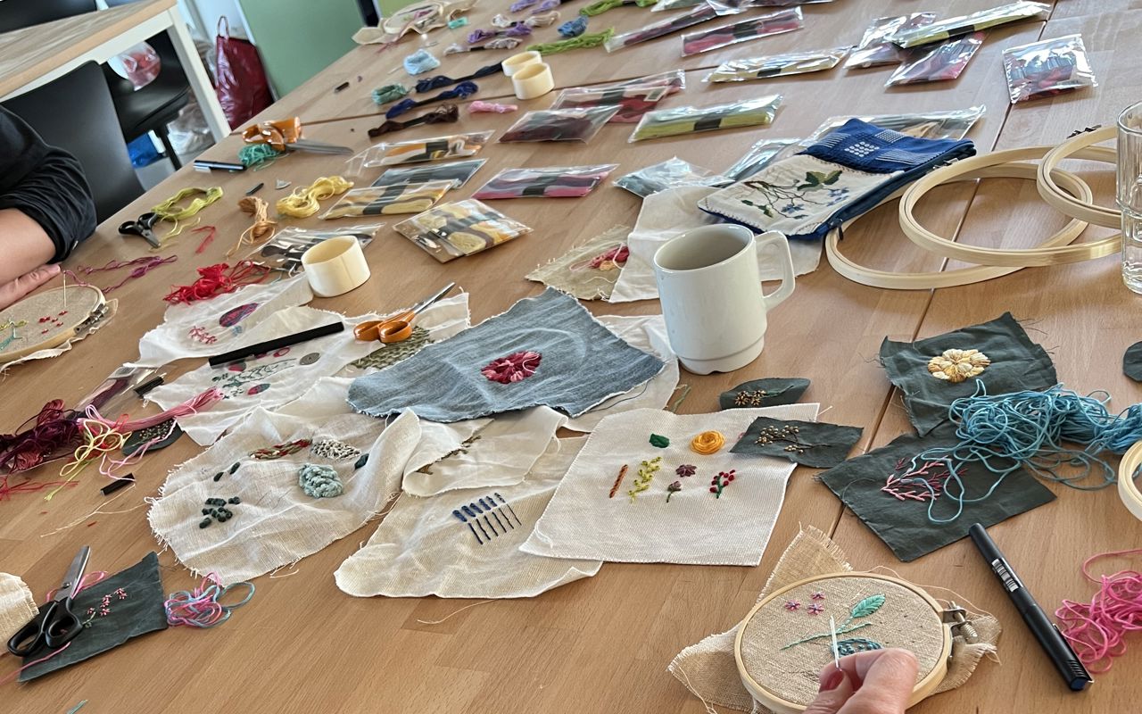Workshop med broderi – bord fyldt med stofstykker, tråd og håndarbejde i gang.