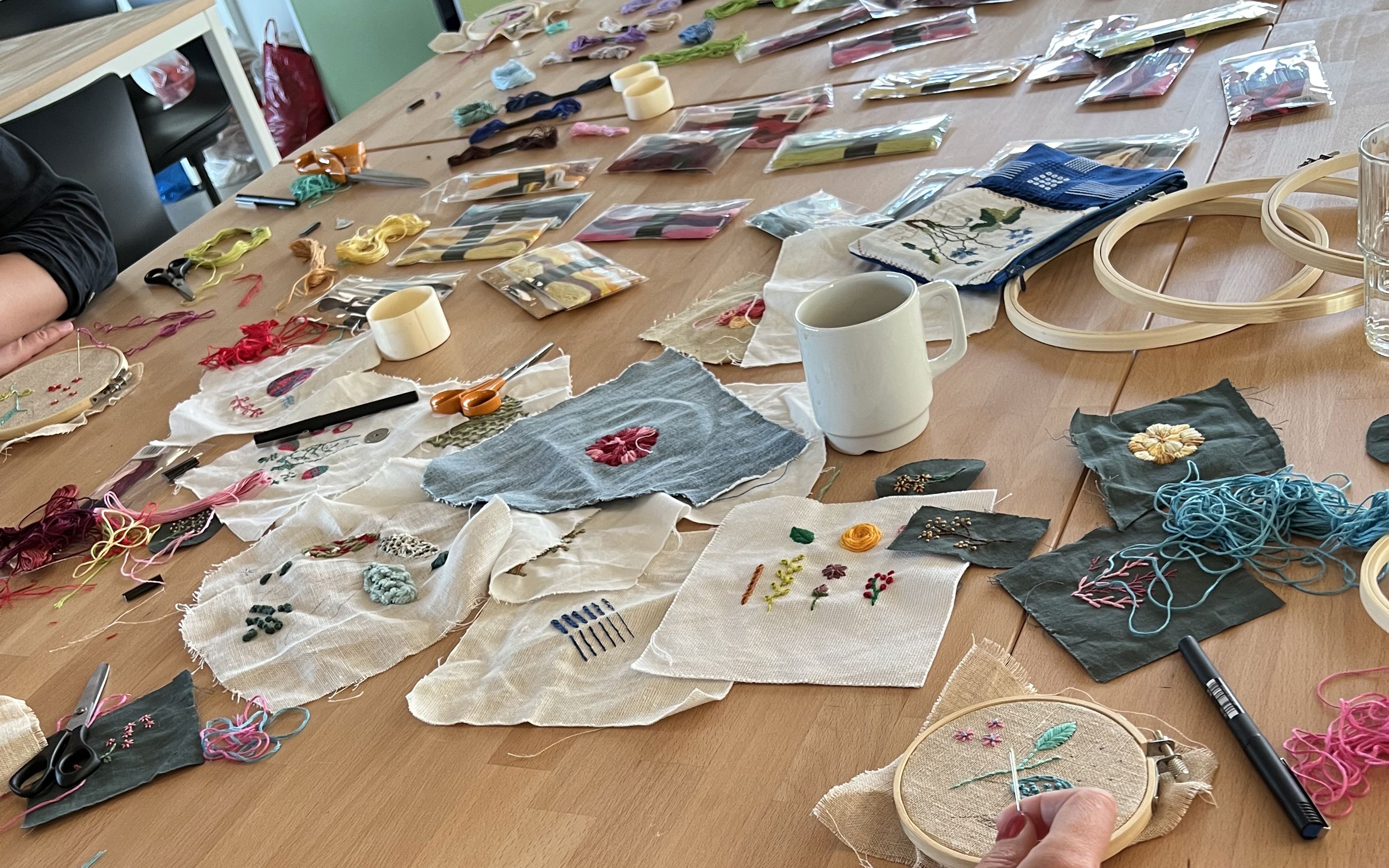 Workshop med broderi – bord fyldt med stofstykker, tråd og håndarbejde i gang.