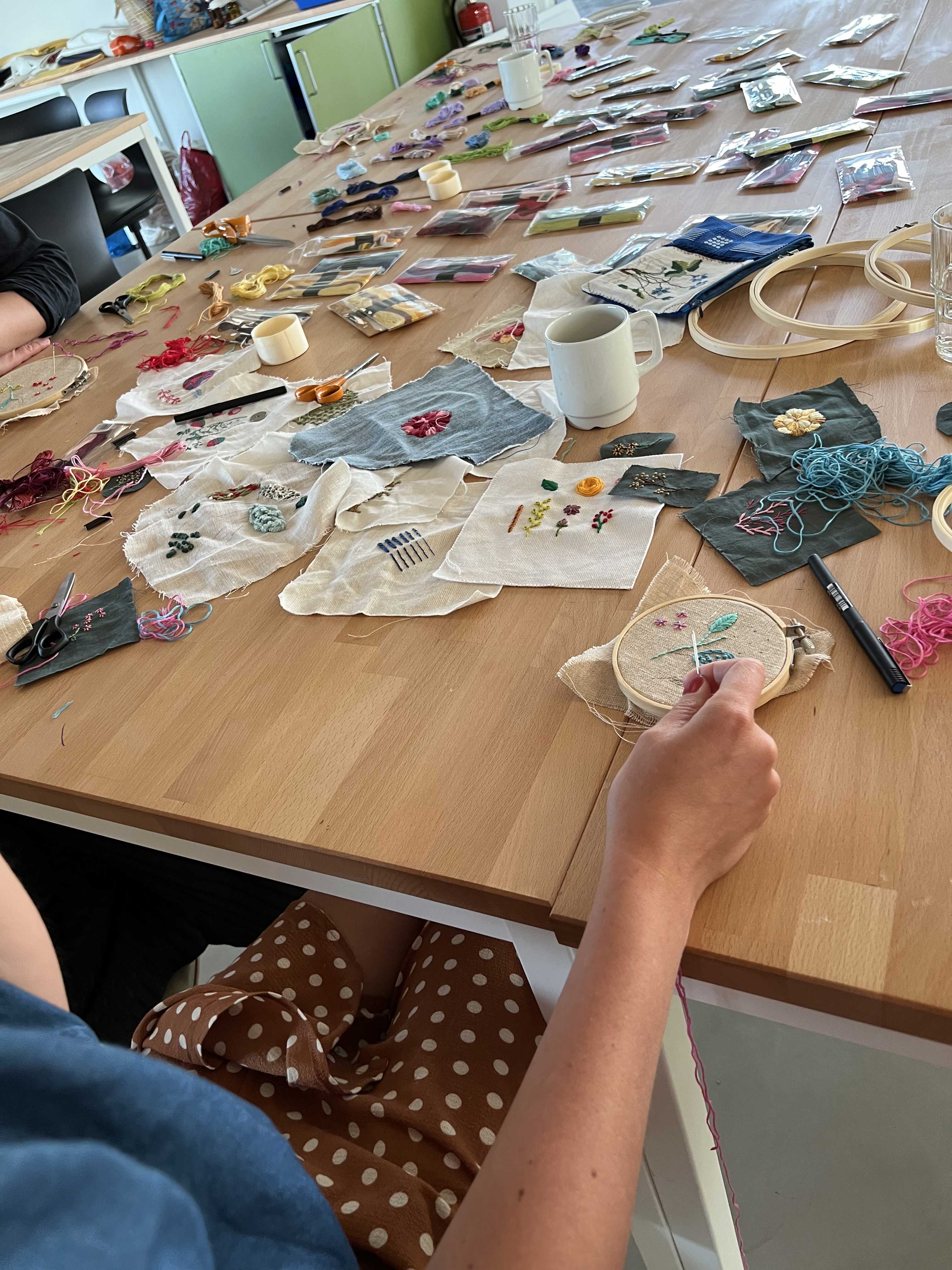 Workshop med broderi – bord fyldt med stofstykker, tråd og håndarbejde i gang.