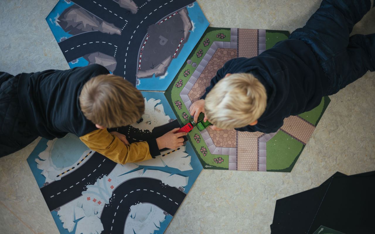 To drenge ligger på gulvet og leger med biler på tre små tæpper med veje