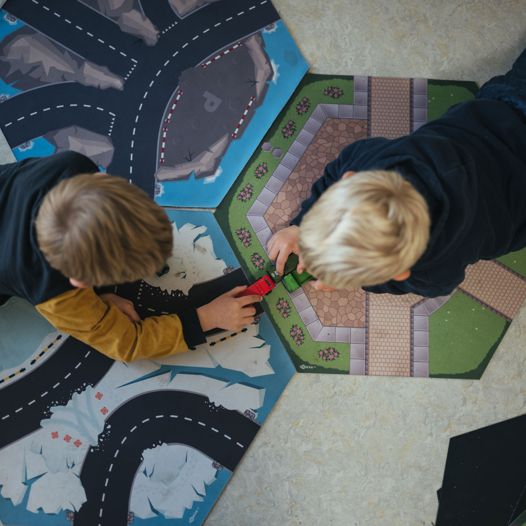 To drenge ligger på gulvet og leger med biler på tre små tæpper med veje