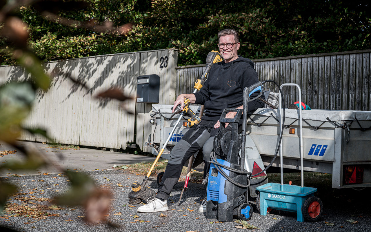 Tomas sidder på kanten af en anhænger og smiler omringet af haveredskaber og værktøj.