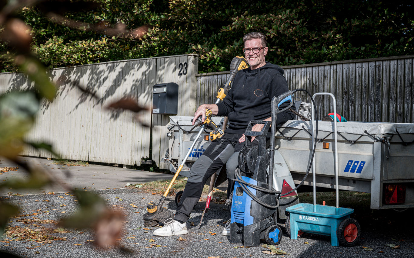 Tomas sidder på kanten af en anhænger og smiler omringet af haveredskaber og værktøj.