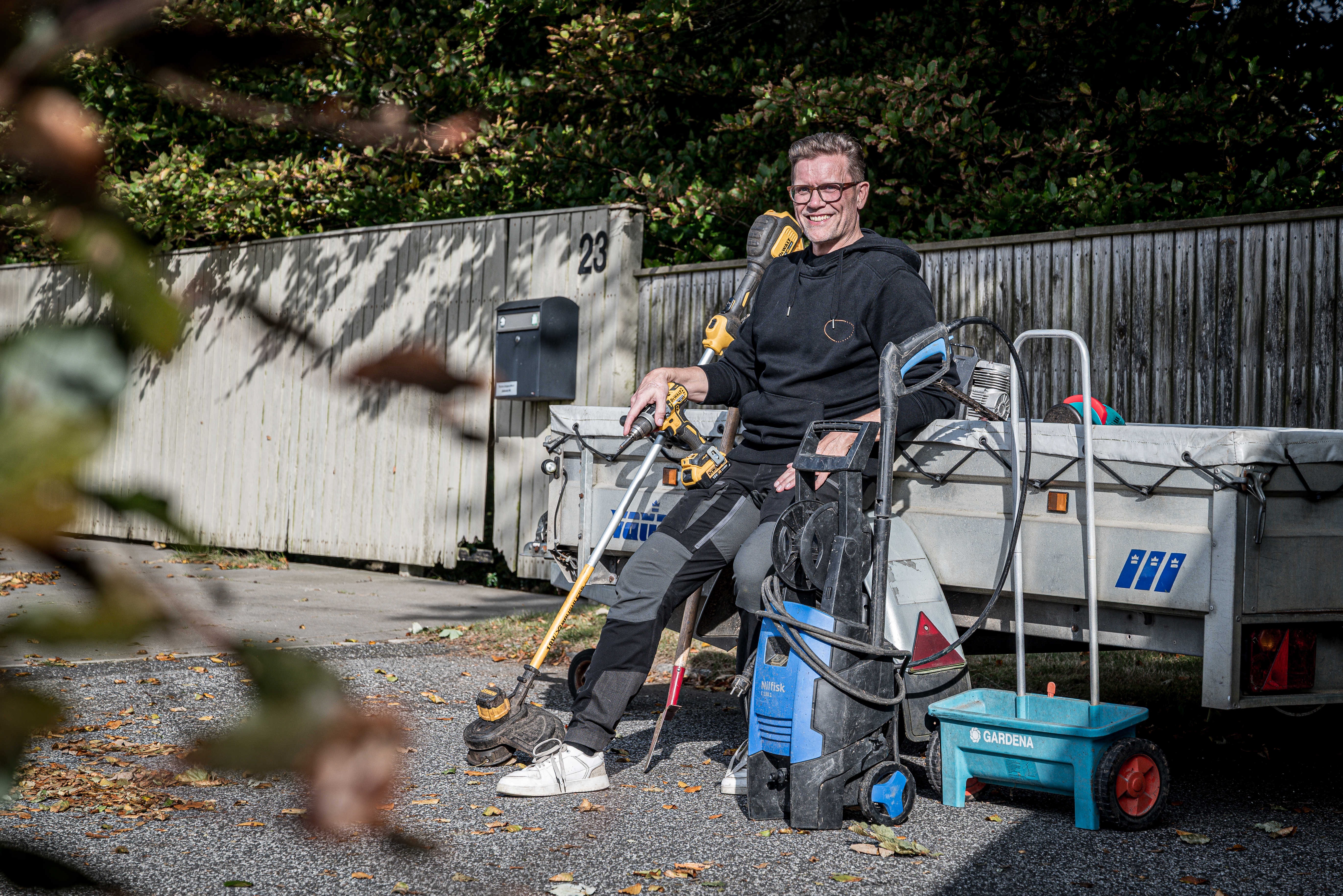 Tomas sidder på kanten af en anhænger og smiler omringet af haveredskaber og værktøj.