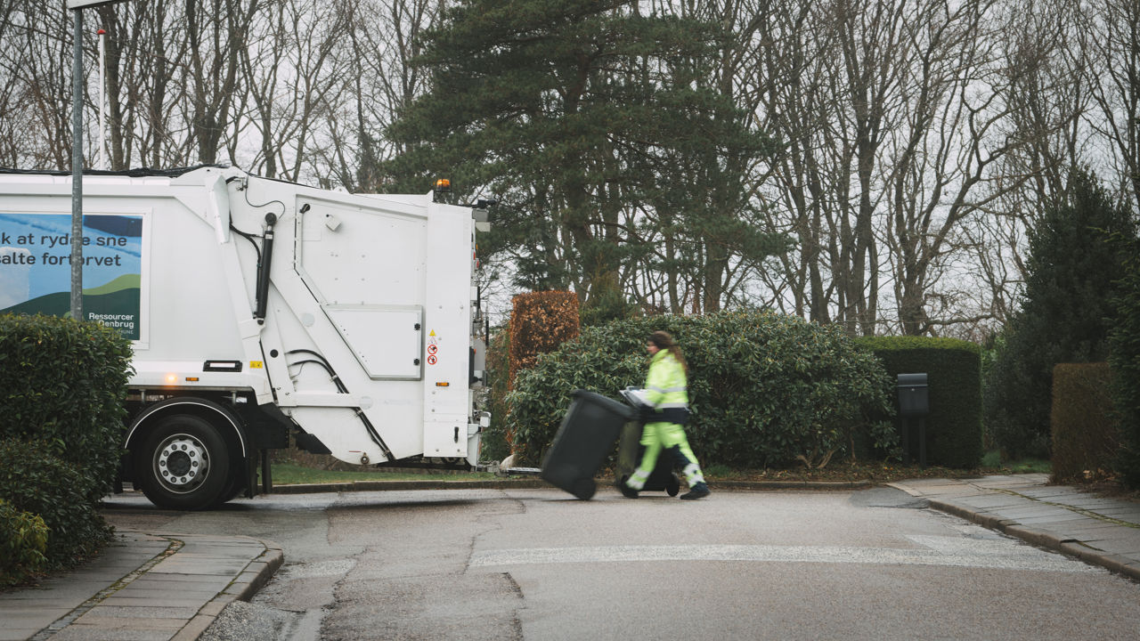 Skraldemand trækker en affaldsbeholder over vejen til skraldebilen på en stille villavej