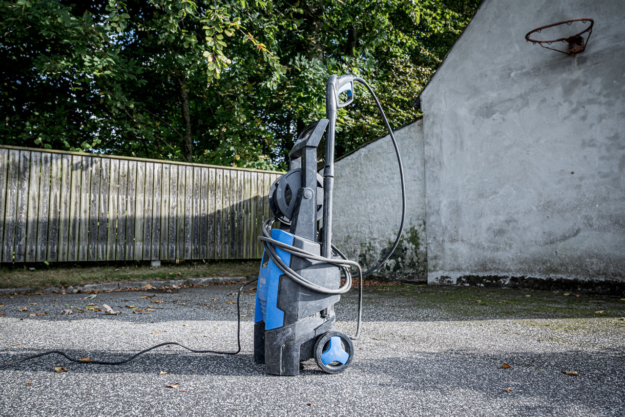 Højtryksrenser placeret på asfalt foran et plankeværk.