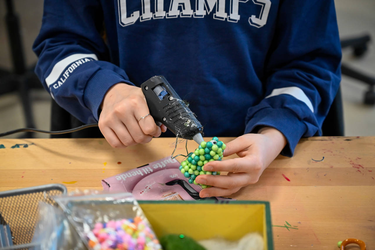Person iført mørkeblå sweatshirt sidder ved arbejdsbord i Laboratoriet på RCV og limer grønne perler sammen med en limpistol.