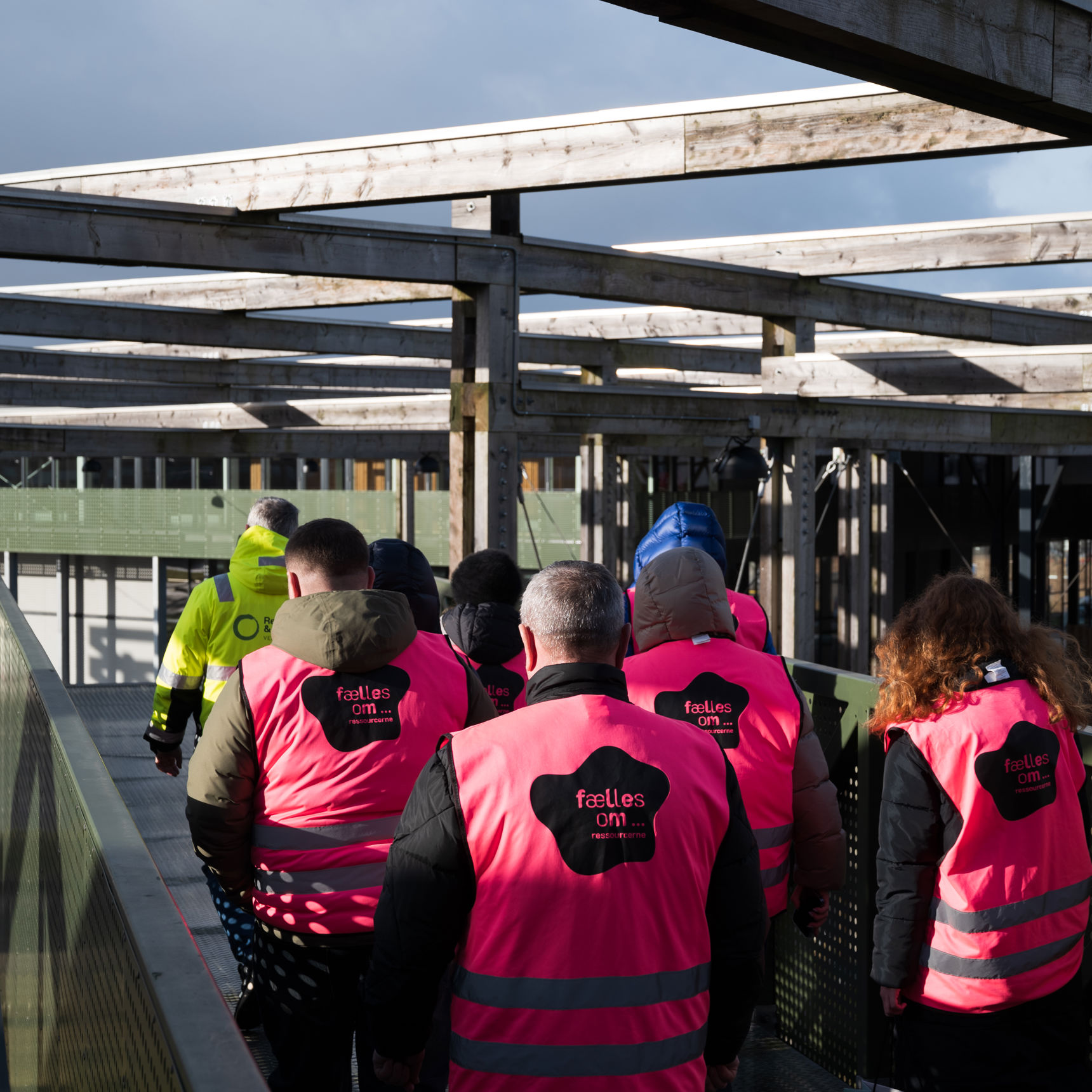 En gruppe mennesker iført pink sikkerhedsveste ses bagfra, mens de går rundt på Læringsbroen på RCV.