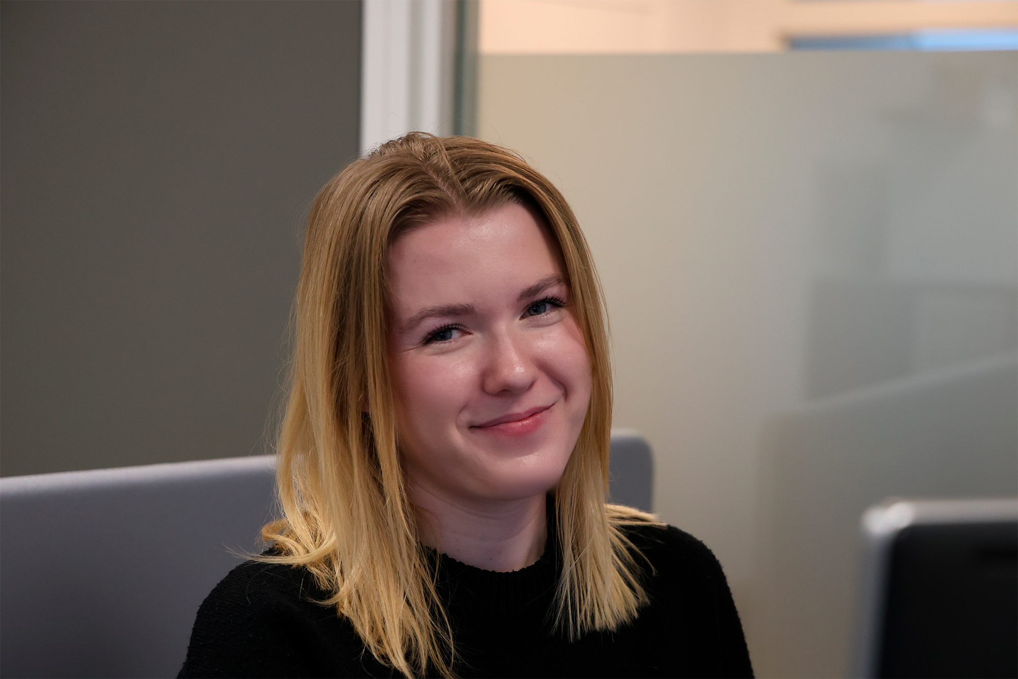 Ung kvinde der sidder og smiler til kameraet.