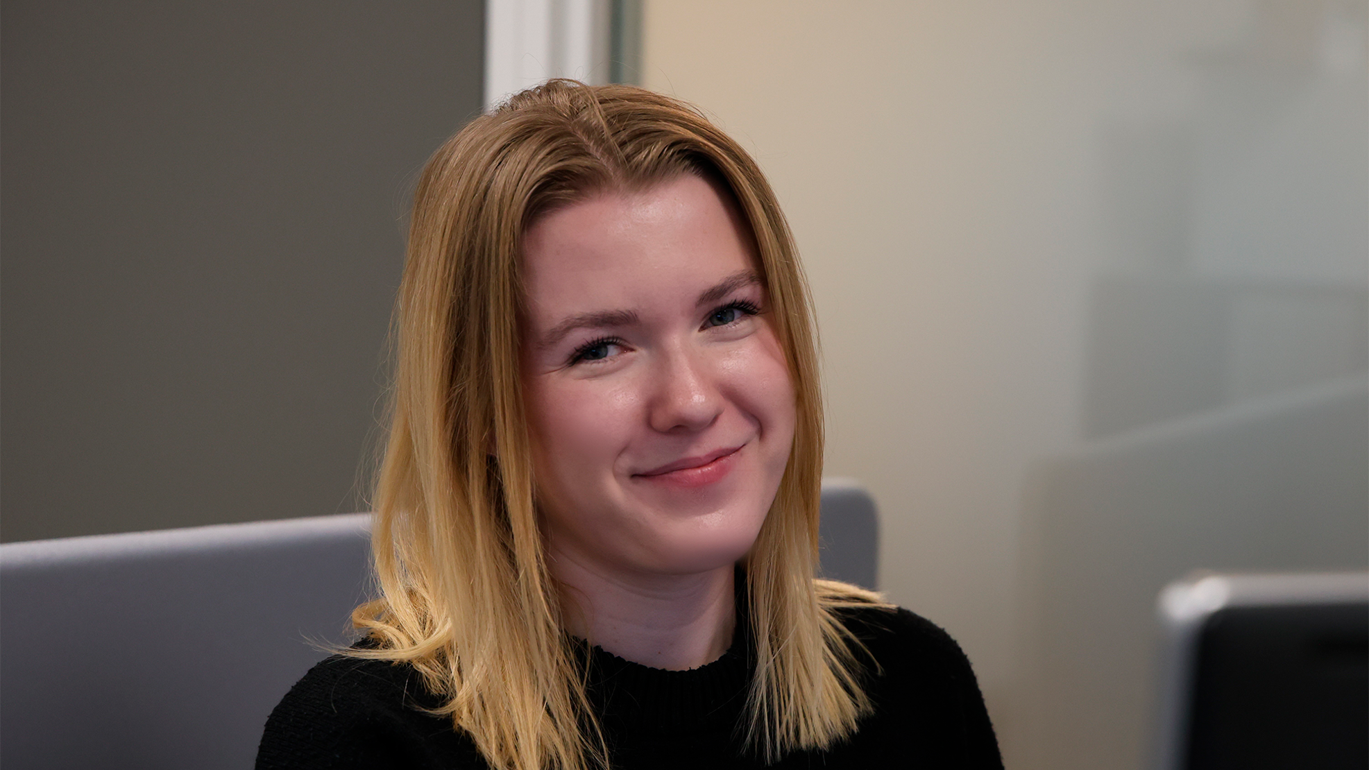 Ung kvinde der sidder og smiler til kameraet.
