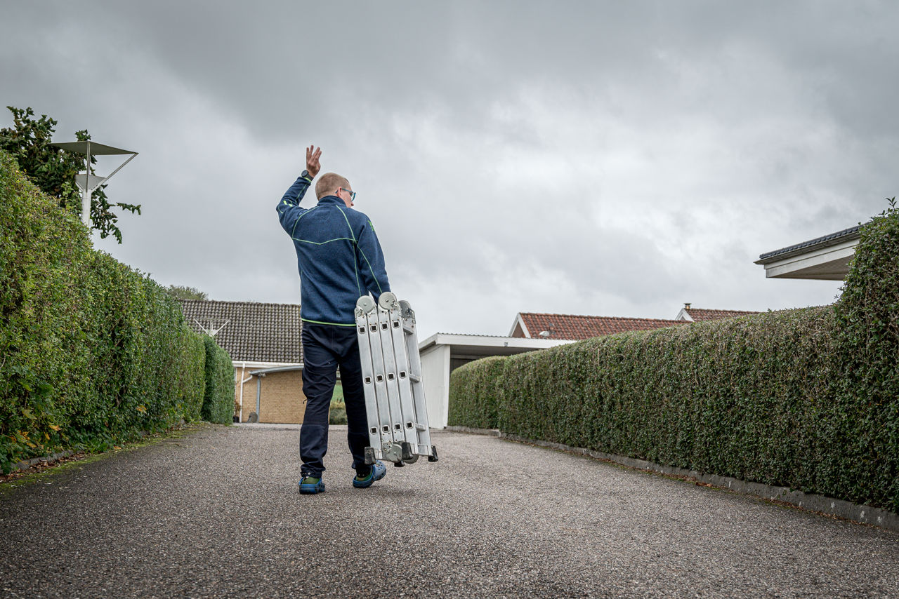 Rasmus vinker til en nabo over hækken, idet han går ned til fællesskuret for at returnere den stige, han har lånt.