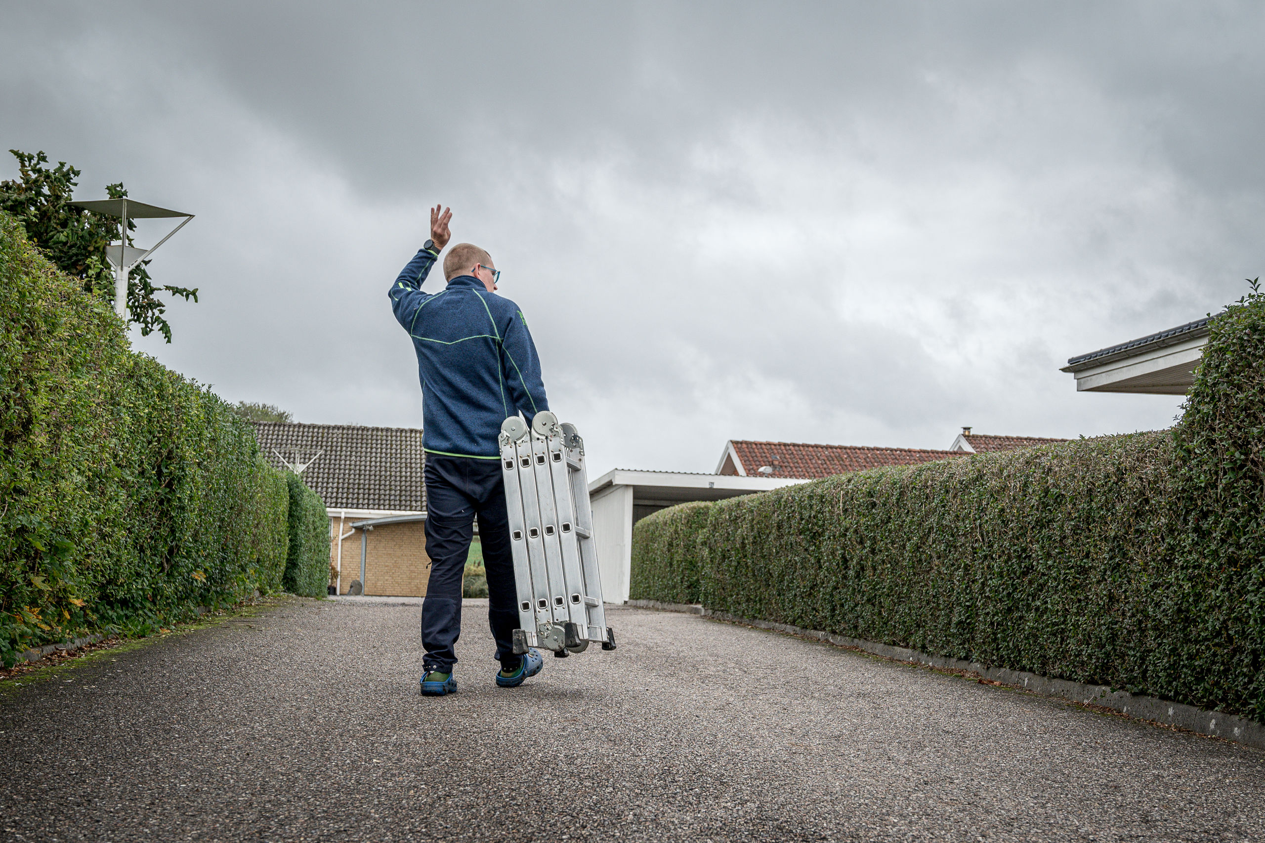 Rasmus vinker til en nabo over hækken, idet han går ned til fællesskuret for at returnere den stige, han har lånt.
