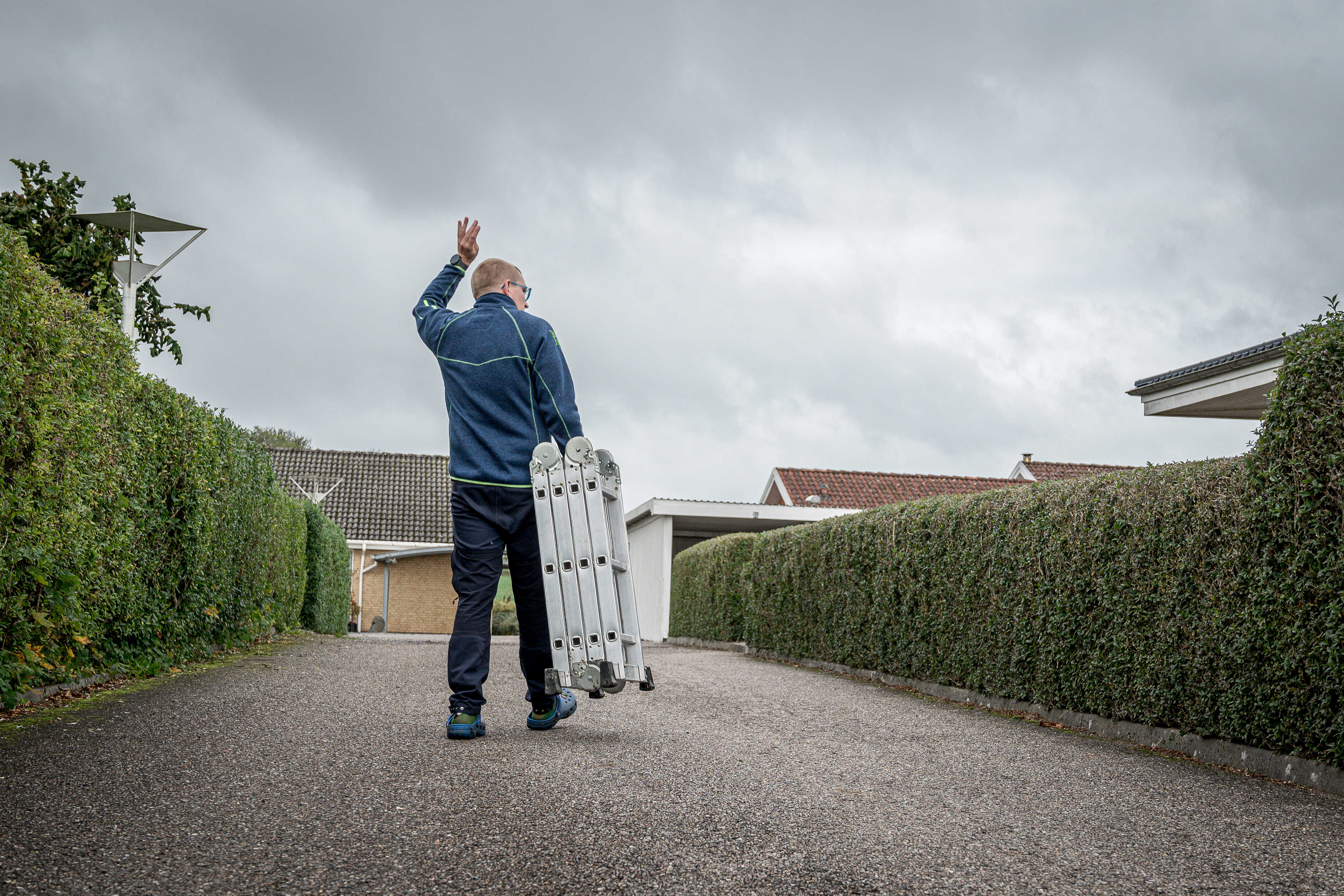 Rasmus vinker til en nabo over hækken, idet han går ned til fællesskuret for at returnere den stige, han har lånt.