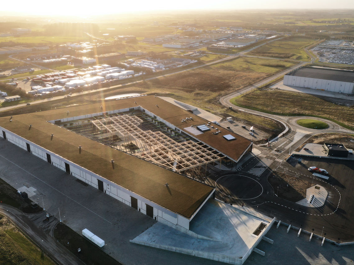 Dronefoto af RessourceCenter Vejle (RCV) med et grønt tag og solpaneler, omgivet af parkeringsplads og grønne områder, der viser centerets bæredygtige arkitektur og indre gårdstruktur.