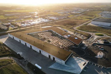 Dronefoto af RessourceCenter Vejle (RCV) med et grønt tag og solpaneler, omgivet af parkeringsplads og grønne områder, der viser centerets bæredygtige arkitektur og indre gårdstruktur.