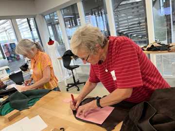 To ældre kvinder ved et arbejdsbord i Laboratoriet på RCV. I gang med at tegne og klippe sy-mønstre i stof.