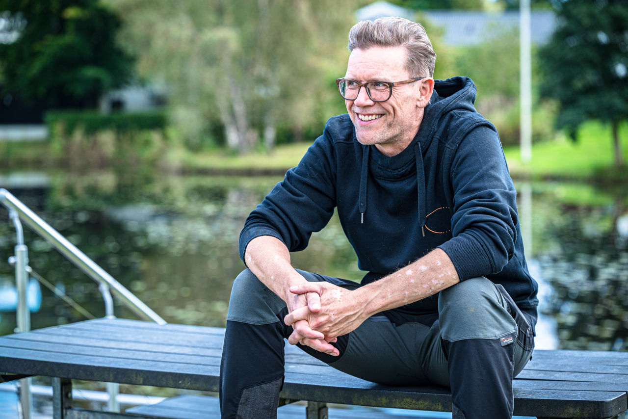 Tomas sidder på en træbænk ved Uhrhøj Sø og smiler.