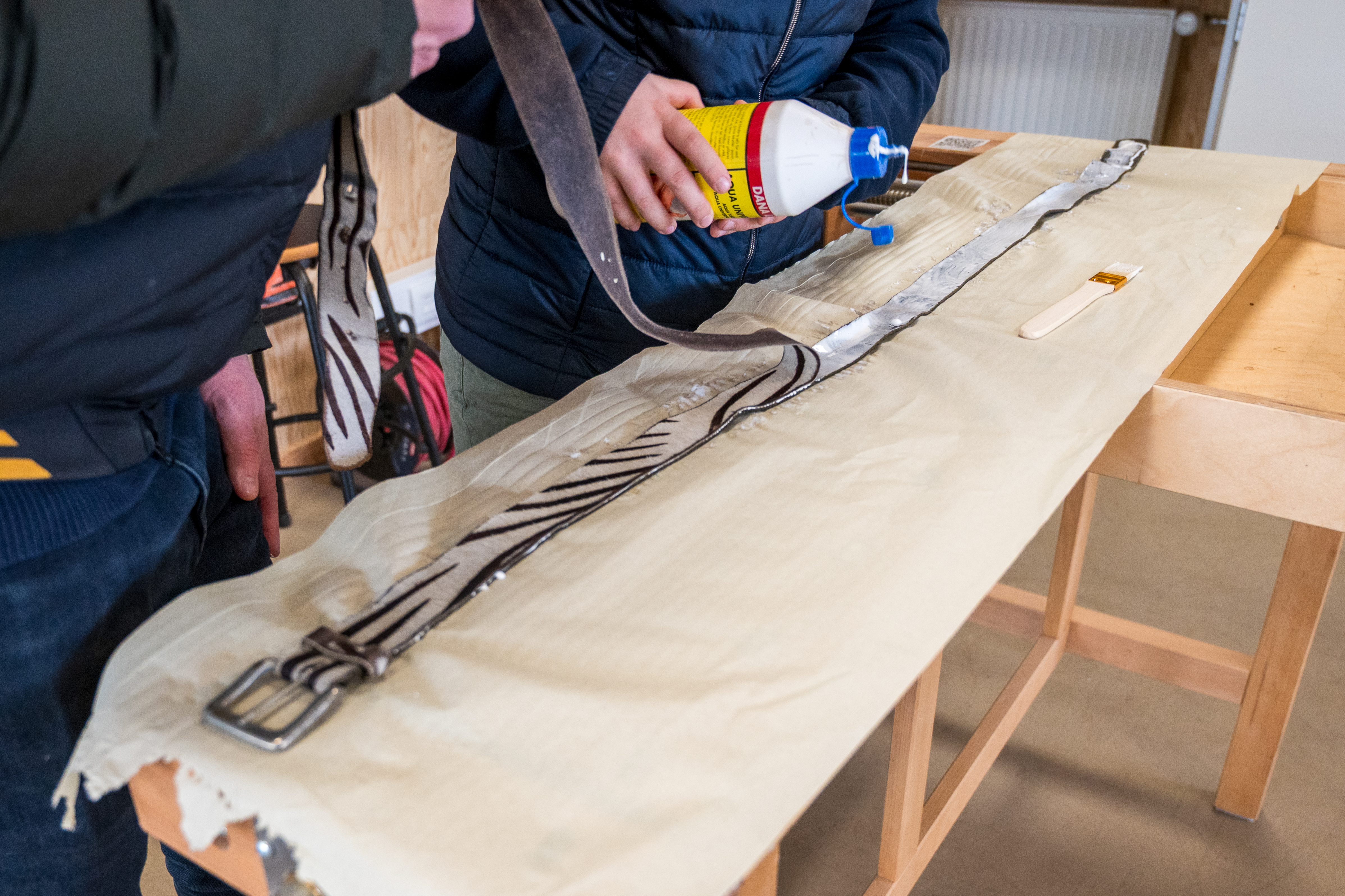 To personer ved arbejdsbord i Laboratoriet i færd med at lime et bælte sammen.