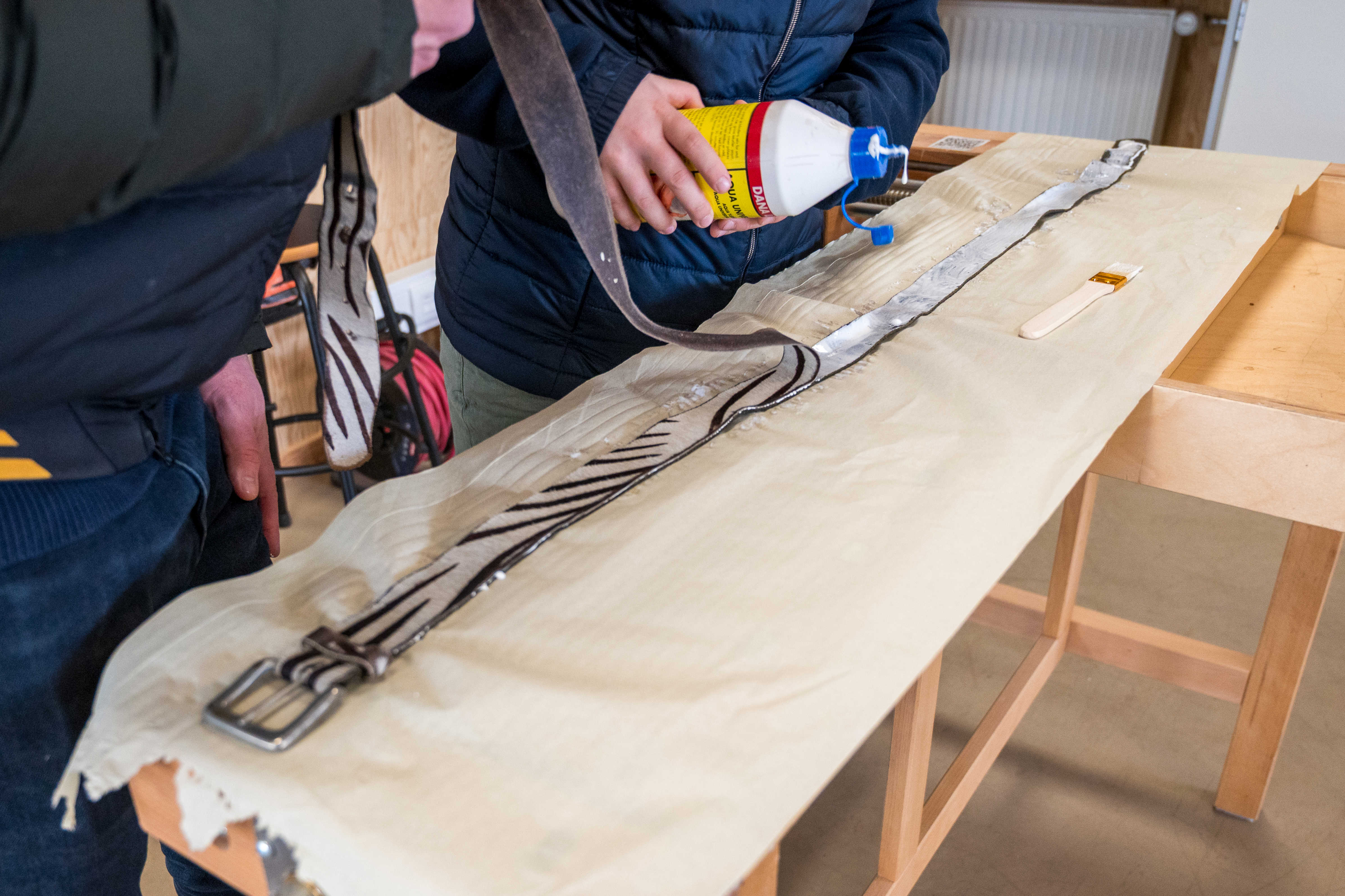 To personer ved arbejdsbord i Laboratoriet i færd med at lime et bælte sammen.