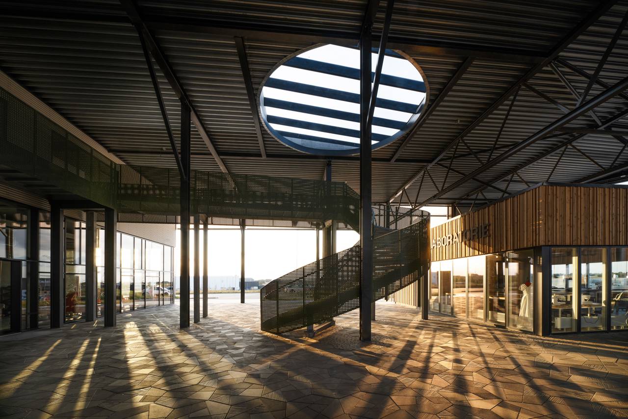 Interiørbillede af RessourceCenter Vejle med moderne arkitektur, cirkulært ovenlysvindue og en spiraltrappe, badet i aftensolens varme lys