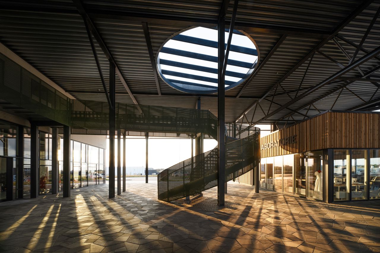 Interiørbillede af RessourceCenter Vejle med moderne arkitektur, cirkulært ovenlysvindue og en spiraltrappe, badet i aftensolens varme lys