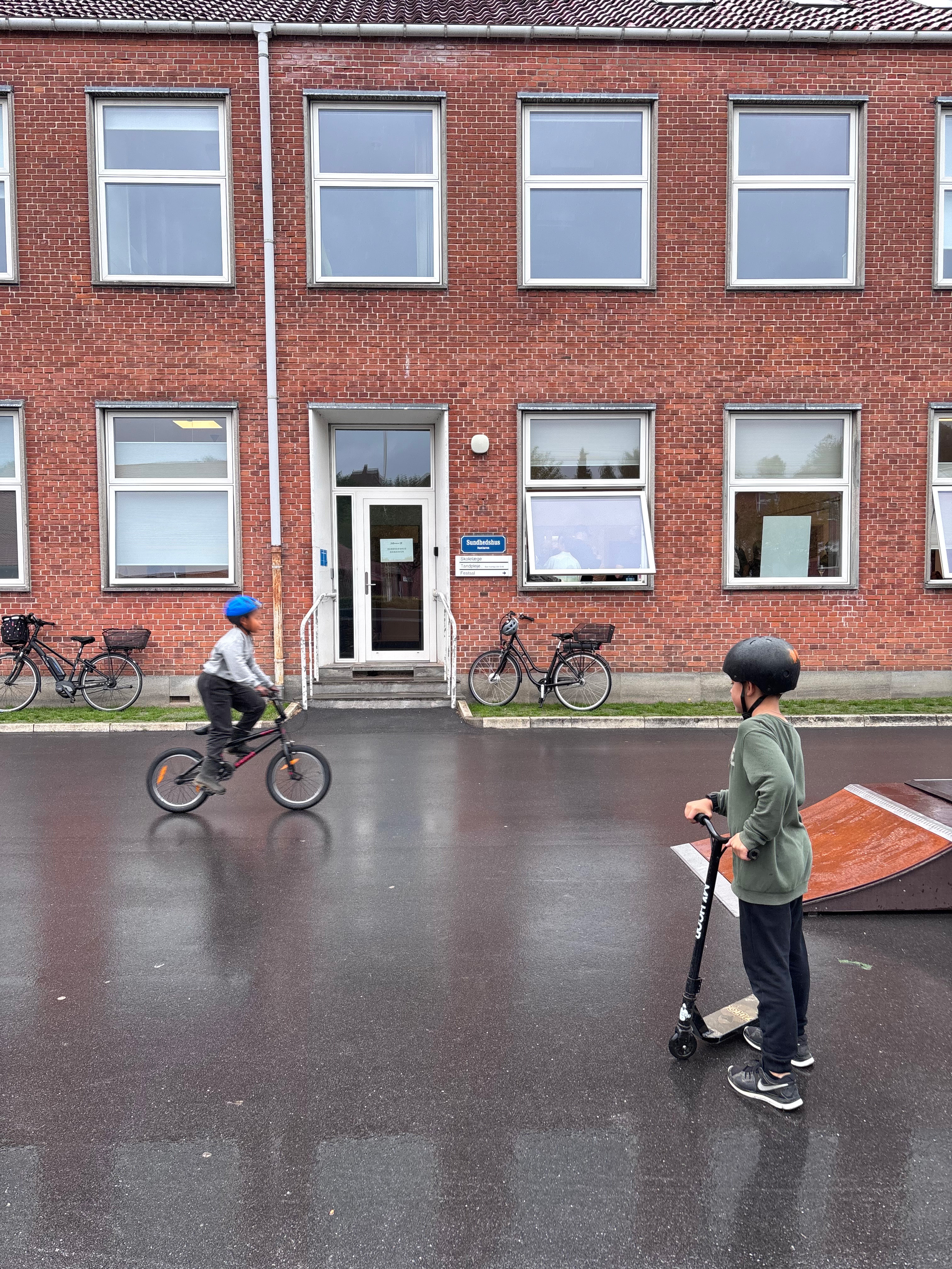 Børn cykler og kører på løbehjul foran Sundhedshus Damhaven