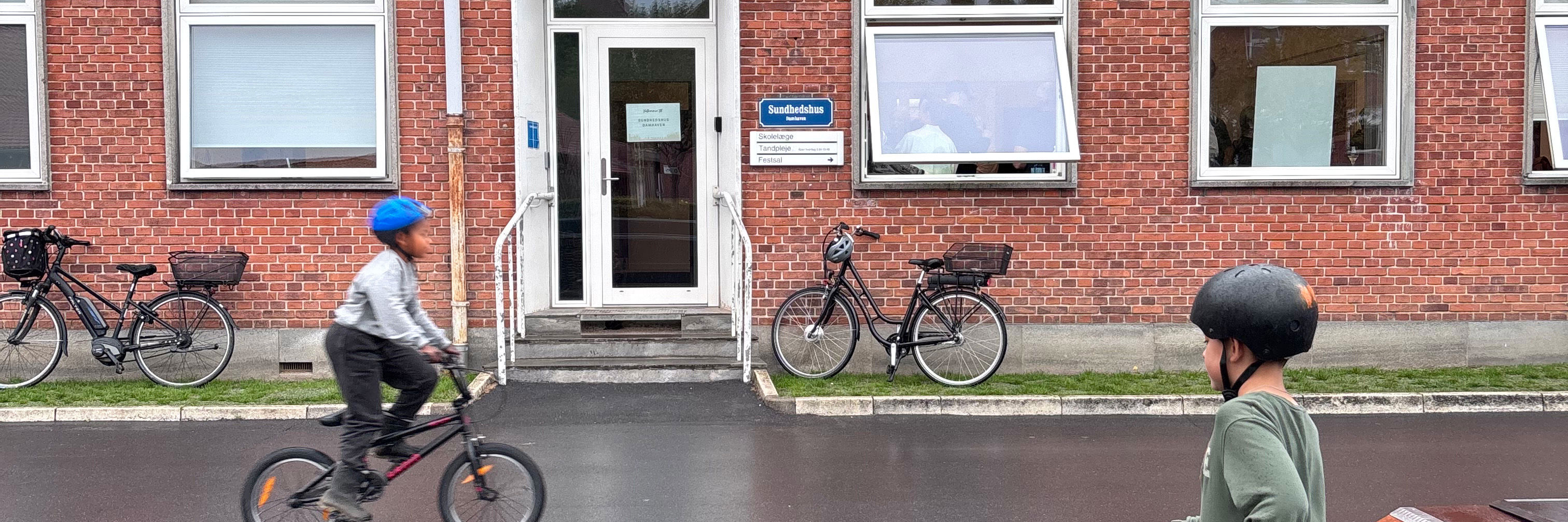 Børn cykler og kører på løbehjul foran Sundhedshus Damhaven