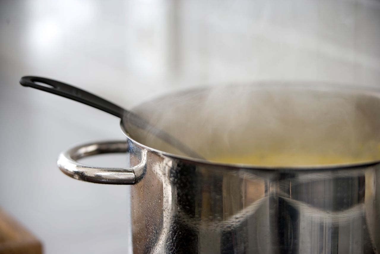 Gryde på komfur med varmt indhold, der damper.