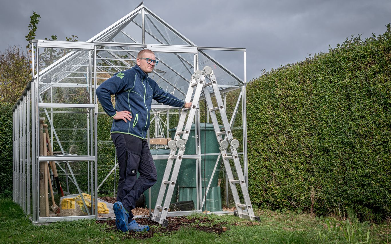 Rasmus med stigen fra fællesskuret foran sit drivhus.